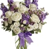 White roses and purple flowers arranged in a glass vase with a purple ribbon