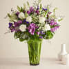 White roses and purple flowers in a tall glass vase