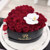 Red roses arranged in a round black box with a white orchid accent