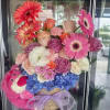 Mixed pink and purple flower arrangement with a plush bear and ribbon