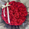 Round bouquet of red roses wrapped in dark paper with a white ribbon