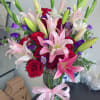 Bouquet of pink lilies and red roses in a glass vase with a pink ribbon