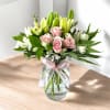 Pink roses and white lilies in a glass vase with a pink ribbon