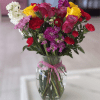 Mixed bouquet of roses and carnations in a glass vase with a pink ribbon