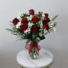 Clear glass vase of red roses with white filler flowers and a red bow.