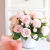 Pink rose bouquet in a white vase with a pink candle and box beside it