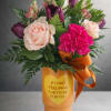 Bouquet of pink and purple flowers in an orange vase with a ribbon