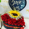 Heart-shaped sign above red roses and a sunflower in a black box