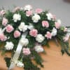 Pink and white floral spray on a casket with ribbon streamers