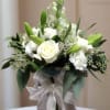 White roses and lilies arranged in a glass vase with a silver ribbon