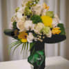 Bouquet of white and yellow flowers with green accents in a black wrap