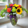 Colorful bouquet with sunflowers, roses, and chrysanthemums in a glass vase