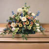 Floral arrangement on a casket with pastel flowers and blue accents