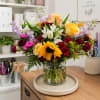 A vibrant, hand-tied arrangement featuring sunflowers, yellow roses, red spray roses, lavender