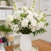 A timeless all-white arrangement featuring white roses, chrysanthemums, stock, and delicate baby&rsquo;s