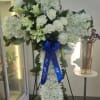 White floral standing spray on an easel with a blue ribbon