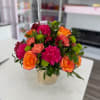 Bouquet of orange roses, pink carnations, and green button mums in a glass vase
