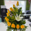 Yellow roses and a white lily arranged in a white vase