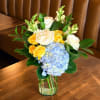 Blue hydrangea and yellow-white rose bouquet in a clear glass vase