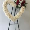 Heart-shaped floral wreath of white roses with a red rose cluster on an easel