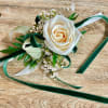 White rose corsage with green and ivory ribbons on a wooden surface