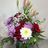 Bouquet of red roses, pink lilies, and purple chrysanthemums in a glass vase
