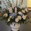 White and blue floral arrangement in a white urn with a small angel figurine