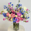 Colorful mixed bouquet of pink, blue, and white flowers in a glass vase