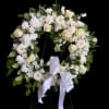 White floral wreath with roses and daisies on a stand, tied with a white ribbon