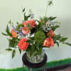 Coral roses, ranunculus, and green dianthus in a clear glass vase on a metal stand