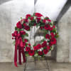 A rich circular wreath of deep red roses, gerbera daisies, and carnations