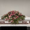 Pink floral spray arranged on top of a white casket