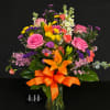 Mixed bouquet of pink, orange, yellow, and purple flowers in a glass vase with an orange ribbon