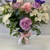 Bouquet of pink, purple, and white flowers in a glass vase with a pink ribbon