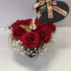Red roses in a black heart-shaped box with white baby's breath and a ribbon bow