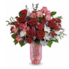 Bouquet of red roses, pink alstroemeria, and white daisies in a pink glass vase