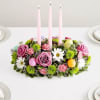 Pink floral centerpiece with three tall candles on a table