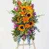 Tall floral spray with sunflowers, lilies, and blue and purple accents on an easel