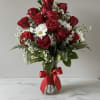 Red roses and white daisies arranged in a glass vase with a red ribbon.