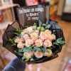 Bouquet of pale pink roses wrapped in black paper with greenery