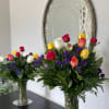 Two mixed-color rose arrangements with purple filler flowers in glass vases on a table.