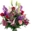 Tall mixed bouquet of red roses, pink lilies, and purple flowers in a clear glass vase