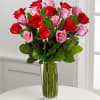 Tall bouquet of red and pink roses arranged in a clear glass vase on a white table