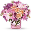 Pink and peach lilies, roses, and mums arranged in a pink glass cube vase