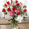 Arrangement of red roses, pink lilies, and white hydrangeas in a clear glass vase