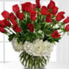 Round vase of red roses arranged above white hydrangeas in a clear glass bowl