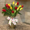 Red and yellow tulips in a gold vase with a white polka dot bow on a countertop