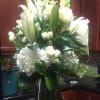 Tall arrangement of white lilies, roses, snapdragons, and hydrangeas in a clear glass vase