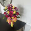 Bright mixed bouquet of pink roses, gerbera daisies, and yellow roses in a clear vase with a yellow and pink bow.