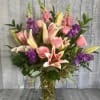 Tall mixed bouquet of pink lilies, pink roses, and purple flowers in a clear glass vase